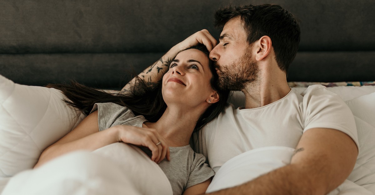 husband kissing wife on forehead in bed